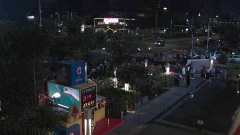 Crowd-gathers-outside-of-buildings-at-intersection-illuminated-by-bright-billboard-at-night