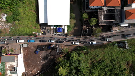 An-Aerial-view-of-heavy-traffic-on-a-narrow-road-in-Canggu,-A-Lot-of-cars-and-scooters-stuck-in-Bali-lined-with-buildings-and-green-areas