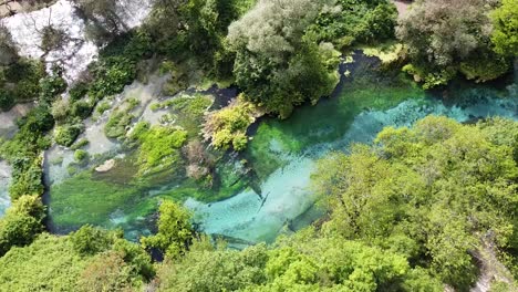 Aerial-view-of-the-Blue-Eye,-a-natural-spring-in-Albania,-showcasing-its-vibrant-blue-and-green-hues-amidst-lush-greenery