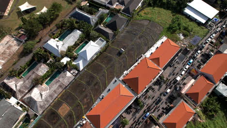 An-orbit-aerial-view-of-Canggu-reveals-a-vibrant-mix-of-busy-streets,-lined-with-cars-and-motorcycles,-and-serene-residential-areas-with-red-roofed-houses-and-rice-field