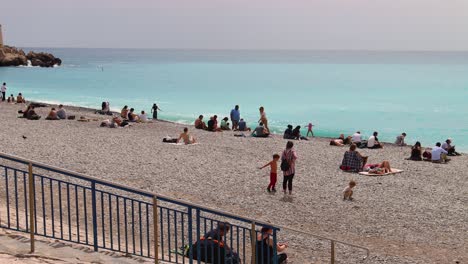 Sunny-day-at-pebble-beach-in-Nice-with-people-relaxing,-swimming-and-enjoying-the-sea