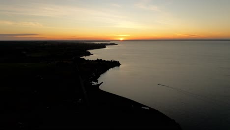 Aerial-serene-sunset-scene-over-a-calm-lake-with-a-silhouetted-coastline-and-gentle-gradients-of-evening-colors