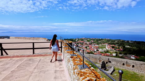 Young,-attractive-woman-overlooking-castle-walls,-the-landscape-in-Greece,-and-the-Mediterranean-Sea