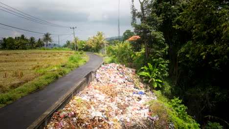 Disgusting-waste-disposal-on-roadside-in-Bali-countryside-near-farm-lands,-drone