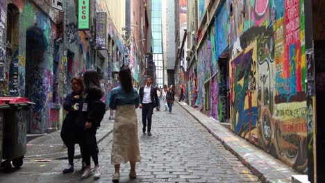 Tourists-touring-at-Hosier-Lane-in-Melbourne-city,-a-popular-cobblestone-laneway-with-a-vibrant-array-of-art-murals-and-graffiti-on-the-exterior-walls-of-buildings,-a-creative-cultural-street-scene