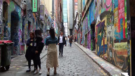 Turistas-Que-Recorren-Hosier-Lane-En-La-Ciudad-De-Melbourne,-Una-Popular-Callejuela-Adoquinada-Con-Una-Vibrante-Variedad-De-Murales-Artísticos-Y-Graffiti-En-Las-Paredes-Exteriores-De-Los-Edificios,-Una-Escena-Callejera-Cultural-Creativa