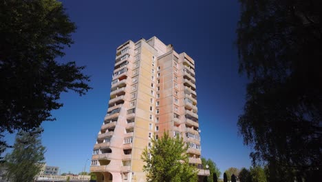 Drone-footage-showcases-a-high-rise-apartment-block-with-balconies-amidst-trees-and-a-blue-sky-during-spring