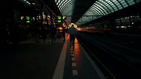 Vista-Trasera-De-Una-Persona-Caminando-Por-La-Plataforma-De-La-Estación-Central-De-Amsterdam-Durante-Una-épica-Puesta-De-Sol-Naranja,-Proyectando-Largas-Sombras-Y-Creando-Una-Atmósfera-Espectacular.