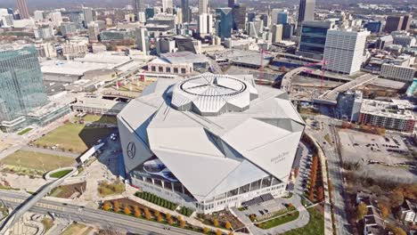 Drone-shot-of-Mercedes-Benz-Stadium-surrounded-by-Downtown-Atlanta-modern-commercial-skyline-and-skyscrapers-buildings-in-autumn-afternoon