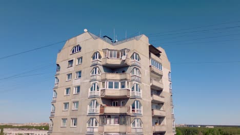 Drone-footage-ascends-past-a-high-rise-grey-Soviet-apartment-block-in-Riga,-revealing-the-city-skyline