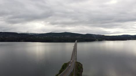 Drone-footage-of-Mjøsbrua-Bridge-spanning-Lake-Mjøsa-near-Moelv,-Norway,-surrounded-by-tranquil-waters-and-scenic-landscapes-under-a-cloudy-sky