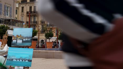 Paintings-On-Street-Backdropped-By-Statue-Of-Lord-Brougham-And-Fountain-In-Cannes,-France,-wide-static-shot