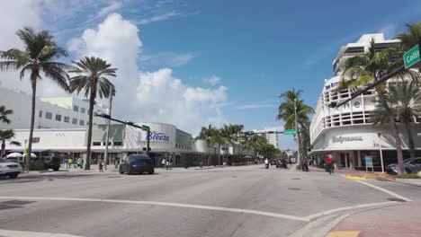 Busy-Miami-street-with-cars,-palm-trees,-and-vibrant-storefronts-under-a-bright-blue-sky