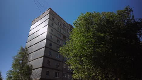 Footage-captures-the-fixed-exterior-of-a-high-rise-residential-flat-block-during-spring,-featuring-a-tree-and-sun-reflections,-highlighting-urban-living-amidst-natural-elements