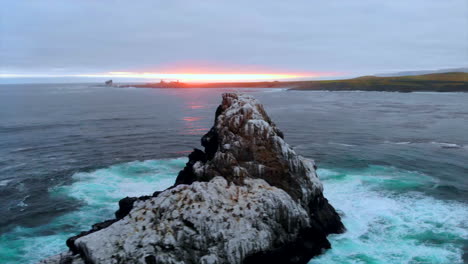 Lovely-sea-view,-drone-dollies-right-past-white-guano-covered-bird-rookery-rock-with-sunset-and-Piedras-Blancas-Lighthouse-on-Central-California-Coast-in-Pacific-Ocean-near-Big-Sur,-4k-Pro-Res-422HQ