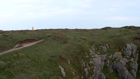 Man-runs-along-a-grassy-path,-smiling-and-looking-at-camera-in-Pembrokeshire-Coast-National-Park