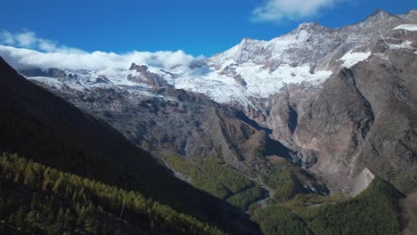 Saastal-Saas-Fee-village-town-Switzerland-aerial-drone-sunny-shadows-stunning-beautiful-Fall-Autumn-Swiss-Alps-mountain-peaks-glacier-surrounding-city-buildings-bridge-Zermatt-Matterhorn-circle-left