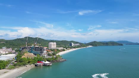 Vuelo-De-Drones-En-Una-Playa-En-Langkawi,-Malasia-Drone-Vuela-Hacia-Atrás-Sobre-La-Vista-Al-Mar-De-La-Naturaleza-Y-El-Edificio-Del-Hotel-En-Construcción