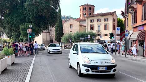 Walking-the-street-crowded-with-people-and-cars,-then-over-the-bridge-Ponet-Pietra-and-overlooking-the-high-river-Adige-and-city-panorama-in-Verona,-Italy