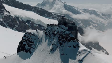 Absteigender-Schwenk-Nach-Oben-Von-Der-Jungfraujochstation-Mit-Wolken-Und-Schneebedeckten-Gipfeln