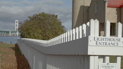 Old-Mackinac-Point-Lighthouse-in-Mackinaw-City,-Michigan-with-cinematic-video-shot-on-dolly-to-reveal-Mackinac-Bridge-and-white-picket-fence-labeled-Lighthouse-Entrance