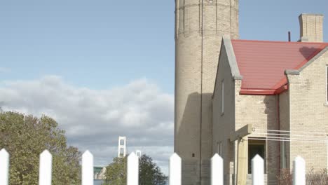 Old-Mackinac-Point-Lighthouse-in-Mackinaw-City,-Michigan-with-cinematic-video-shot-tilting-down-to-reveal-Mackinac-Bridge-and-white-picket-fence