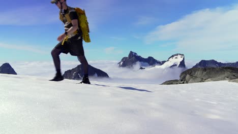 Staic-shot-of-mountaineer-hiking-on-a-snowpatch-above-the-clouds-whilst-looking-at-the-majestic-peaks-in-the-background