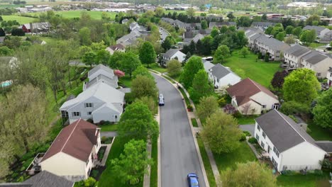 Blue-car-driving-on-street-in-green-neighborhood-of-USA