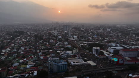 AERIAL:-Hazy-sunset-in-downtown-San-Jose-city,-in-Costa-Rica,-Central-America