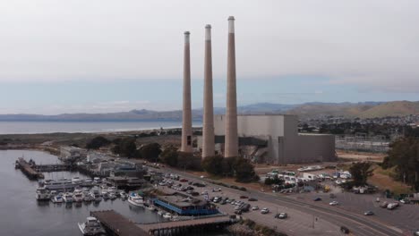 Low-rising-aerial-shot-of-the-three-famous-smokestacks-towering-above-the-defunct-Morro-Bay-Power-Plant-in-Morro-Bay,-California