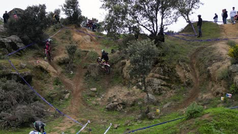 Drohnenflug-In-Einer-Outdoor-Motocross-Meisterschaft,-Bei-Der-Der-Pilot-Auf-Der-Markierten-Strecke-In-Aktion-Ist,-Der-Berater-Des-Piloten-Da-Ist-Und-Es-Leute-Gibt,-Die-Zuschauen-Und-Spaß-Haben