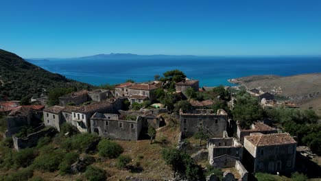 Charming-Village-with-Traditional-Stone-Houses-Built-on-a-Hill-Overlooking-the-Ionian-Sea,-Beautiful-Valley-with-Mediterranean-Olive-Trees-in-Albania
