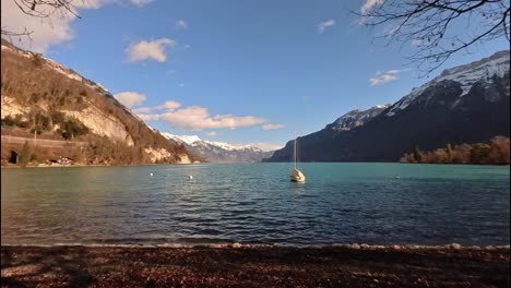 A-slow-panning-of-the-Bringer-lake,-showing-the-water,-a-sailboat-anchored-and-the-mountains-with-snow-at-the-background