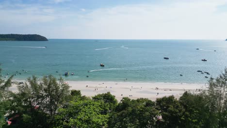 drone-flight-at-a-beach-in-langkawi,-malaysia-drone-flies-over-a-building-towards-the-sea-white-beach,-blue-sea-and-boats-cruising-by-the-water