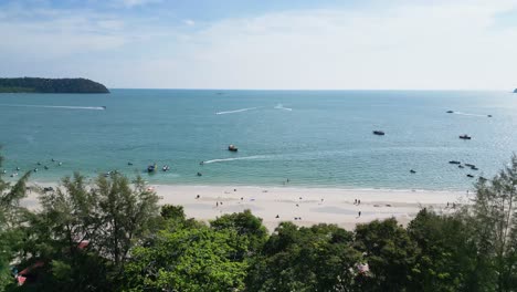 Vuelo-De-Drones-En-Una-Playa-En-Langkawi,-Malasia-Drone-Vuela-Sobre-Un-Edificio-Hacia-El-Mar-Playa-Blanca,-Mar-Azul-Y-Barcos-Navegando-Por-El-Agua