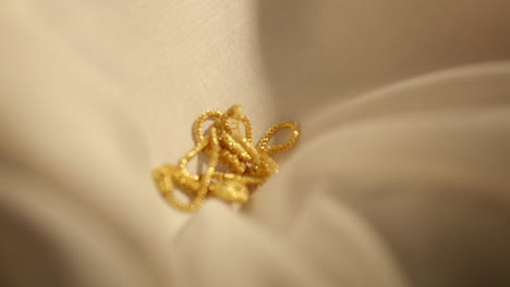 Wunderschöne-Goldkette-Mit-Herzanhänger,-Die-In-Zeitlupe-über-Beigen-Stoff-Gleitet
