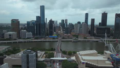 Wheel-of-Brisbane-City-Brissy-South-Bank-Park-Australia-aerial-drone-tall-skyscraper-skyline-River-bus-Go-Between-William-Jolly-Story-Bridge-Quay-ferry-boats-cloudy-Aussie-autumn-winter-forward-pan-up