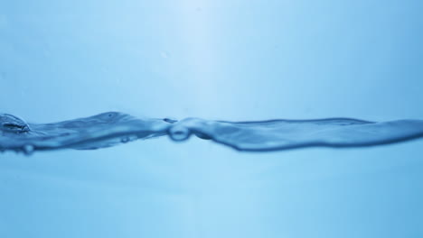 Waves-of-crystal-clear-blue-mineral-water,-creating-some-tiny-bubbles-and-droplets-of-in-a-water-tank