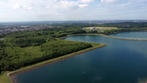 Aerial-view-high-above-water-supply-reservoir-blue-sky-reflections-in-rural-countryside-lake