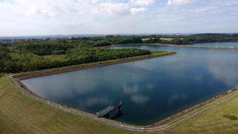 Aerial-view-rise-above-water-supply-reservoir-idyllic-blue-sky-reflections-in-rural-countryside-lake