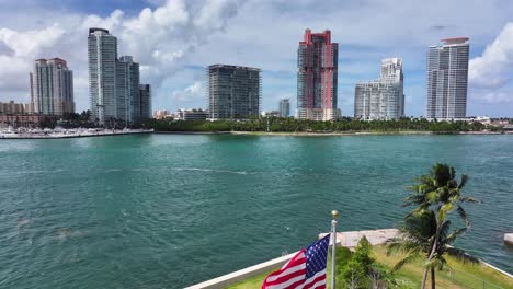 Banderas-De-Estados-Unidos-Y-Fisher-Island-Ondeando-En-Miami,-Florida