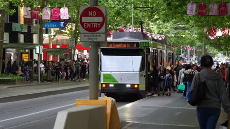 Passengers-boarding-the-tram-at-the-stop-on-Bourke-Street-Mall-and-Swanston-street,-with-cyclists-riding-across-the-bike-lane-in-the-bustling-Melbourne-central-business-district