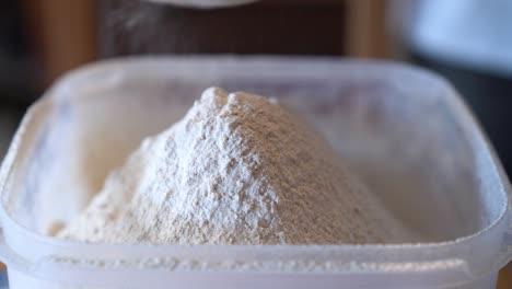 Flour-being-poured-into-a-clear-plastic-container,-creating-a-small-mound-of-fine-powder