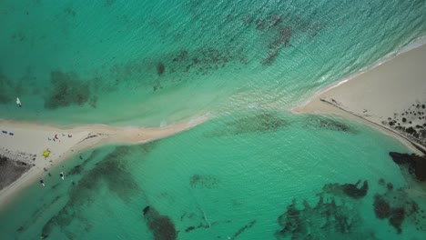 A-sandy-passage-connecting-two-turquoise-beaches-with-people-enjoying-the-water,-aerial-view