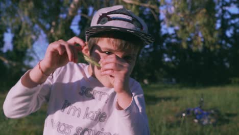 Close-up-footage-of-cute-5-years-old-caucasian-boy-staring-at-the-camera-and-playing-with-an-ear-of-wheat-outdoors-4K