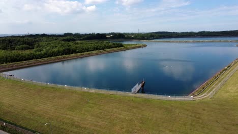 Vista-Aérea-Dolly-Shot-Depósito-De-Suministro-De-Agua-Cielo-Azul-Reflejos-En-El-Lago-Rural