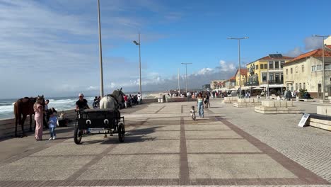 Punto-De-Vista-De-Los-Turistas-Que-Controlan-Los-Paseos-A-Caballo-Y-Los-Lugareños-Caminando-Por-La-Calle-En-Un-Hermoso-Día-En-Praia-Do-Furadouro,-Ovar,-Portugal