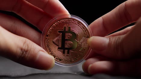 Hands-Holding-Bitcoin-Crypto-Currency-in-Plastic-Coin-Case-Against-Dark-Background,-Close-Up