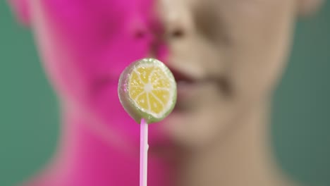 Young-woman-sucks-a-lime-flavored-lollipop,-close-up-face-studio-shot