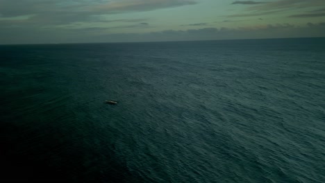 Wide-dramatic-aerial-pan-of-lone-boat-on-open-wavy-blue-ocean-on-cloudy-day